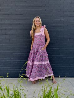 a woman standing in front of a brick wall wearing a pink and purple floral dress