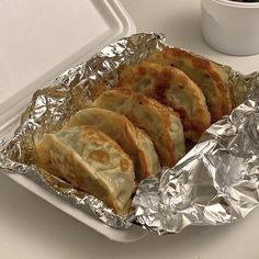 some food is sitting on tin foil next to a white cup and sauce in a styrofoam container