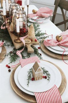 a table set for christmas with plates, napkins and candle holders on the tables