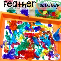 an orange tray filled with paint and colorful feathers