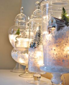 christmas decorations in glass jars with lights on the top and snow around them, along with small trees