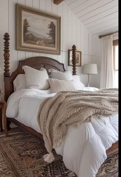 a bed with white sheets and pillows in a bedroom next to a window, rugs and two lamps