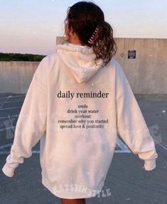 a woman wearing a white hoodie with the words daily reminder printed on her back