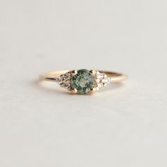 a green and white diamond ring with three diamonds on the side, set in yellow gold