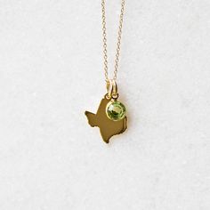 a gold plated necklace with a green crystal in the shape of a state on it