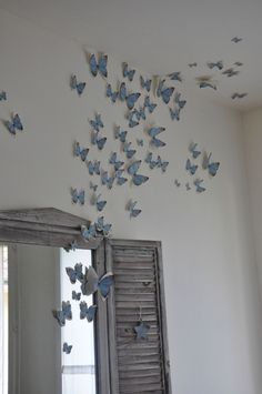 the butterflies are flying from the ceiling to the wall in the room, and there is a mirror on the floor next to it