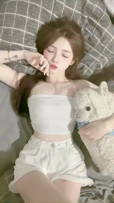 a woman laying in bed with a stuffed animal next to her chest and wearing a white top