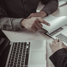 two people sitting at a table with papers in front of them, one pointing to the page