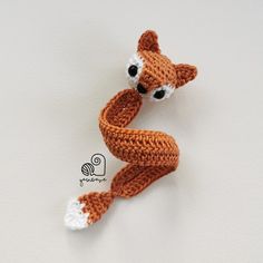 a crocheted fox brooch sits on a white surface with the tail curled up