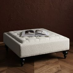 a white ottoman with an open book sitting on it's legs in front of a brown wall