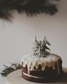 a cake with icing and decorations sitting on top of a wooden plate next to a pine tree