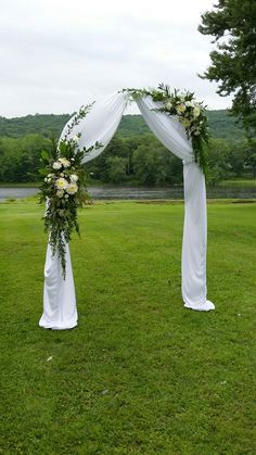 an outdoor wedding ceremony setup with white drapes and greenery on the grass area