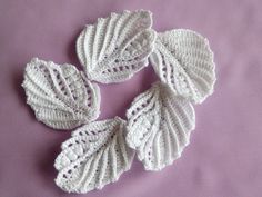 three crocheted leaves on a purple surface, one is white and the other is beige