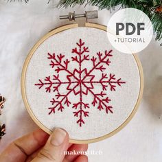 a hand embroidered snowflake is shown in front of a pine tree with cones