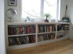 a bookshelf filled with lots of books in front of two window sills