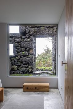 a room with a stone wall and large window in the center, next to a wooden bench