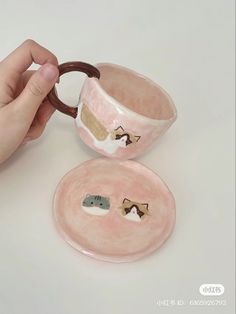 a hand holding a pink ceramic cup and saucer with two small animals on it