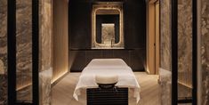 a massage room with a white table and stool in the middle, surrounded by marble walls