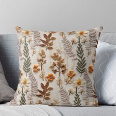 an embroidered pillow with flowers and leaves on the front, sitting on a couch next to pillows