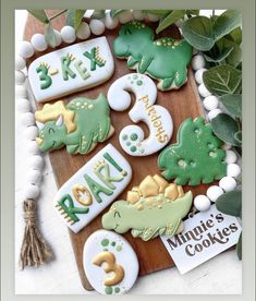 decorated cookies on a cutting board with name tags and numbers in the shape of dinosaurs