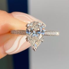 a close up of a person's hand holding a ring with a pear shaped diamond