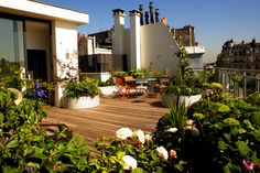 an outdoor deck with potted plants and flowers on the ground next to buildings in the background