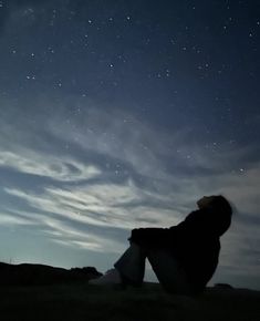 a person sitting on the ground looking up at the sky with stars in the background