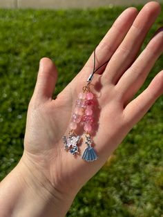 a hand holding some pink beads on it's palm in front of green grass