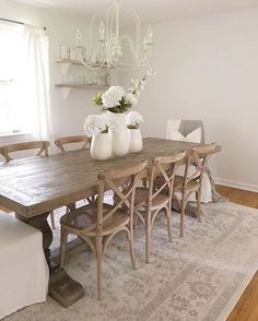 a dining room table with white vases on top of it and chairs around it