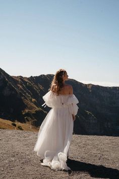 a woman in a white dress standing on top of a mountain