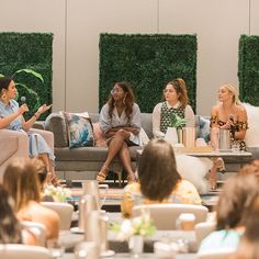 four women sitting on couches talking to each other in front of a group of people