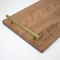 a wooden cutting board with a brass handle and engraved name on the bottom, along with a gold pen