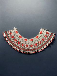 an old necklace with red and white beading on the bottom, sitting on a black surface