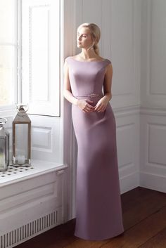 a woman standing in front of a window wearing a long purple dress with an asymmetrical neckline