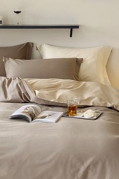 an open book on a bed with sheets and pillows next to a glass of whiskey