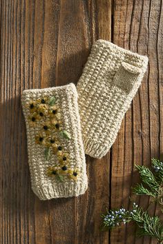 two crocheted mitts sitting on top of a wooden table next to flowers