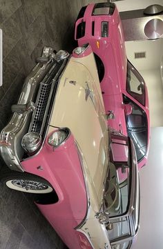 a pink and white car is parked in a showroom with its hood up open