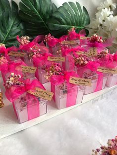 small boxes with pink bows and tags on them are sitting on a table next to flowers