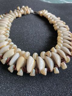 a necklace made out of shell beads on a black surface with white and brown accents