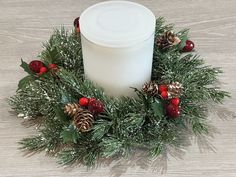 a white candle surrounded by greenery and pine cones