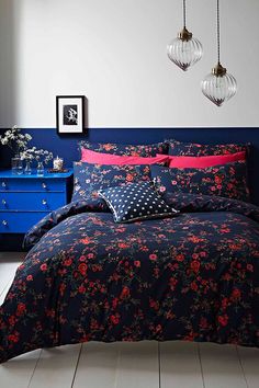 a bedroom with blue and red bedding, two hanging lights and a dresser in the corner