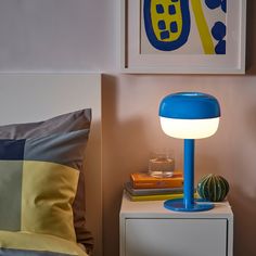 a blue lamp sitting on top of a table next to a white nightstand with books