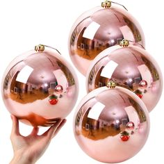 four shiny pink christmas balls with reflections on them are being held by a person's hand