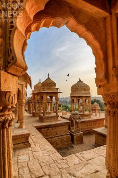 an archway leading to several pavilions with birds flying in the sky