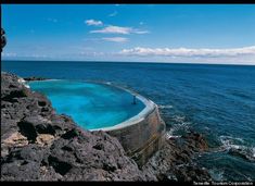 a man standing on the edge of a cliff next to an empty pool in the ocean