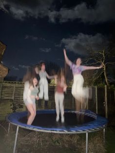 some people are jumping on a trampoline in the yard at night with their arms up