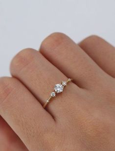 a woman's hand wearing a gold ring with two diamonds on it and one diamond in the middle