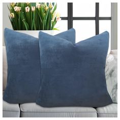 two blue pillows sitting on top of a white couch next to a vase with flowers