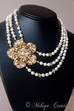 This Elegant and unique one of a kind wedding necklace will make a gorgeous accessory for a Bride. Perfect for a woman that wants luxury with a vintage-inspired flair. Three strands of hand knotted white Swarovski pearls and crystals are mixed to create a little twinkle.  Hand weaved into the filigree focal piece with anti-tarnish-gold wire is Clear and Golden Shadow Swarovski crystals, white pearls and rhinestones. The piece just sparkles with fire in any light.  Some of the delicate detail get Exquisite Gold Wedding Necklaces, Exquisite Pearl Wedding Necklace, Exquisite Pearl White Wedding Necklace, Exquisite Gold Wedding Necklace, Exquisite Pearl Necklace With Elegant Design For Wedding, Elegant Crystal Pearl Necklace For Wedding, Elegant Gold Backdrop Necklace For Wedding, Handmade Elegant Pearl Necklace For Wedding, Pearl White Crystal Bridal Necklace For Wedding