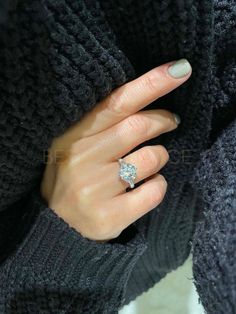 a woman's hand with a diamond ring on her finger, wearing a black sweater